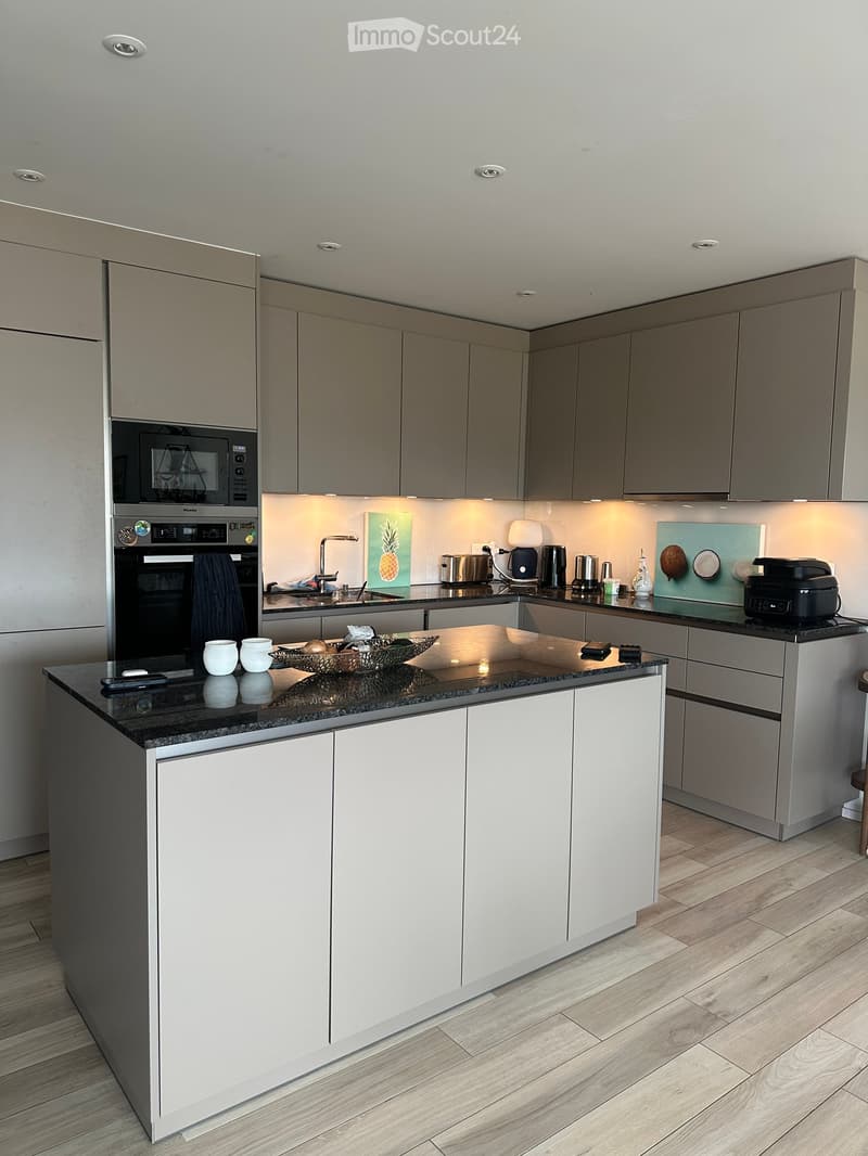 Modern kitchen with grey and white cabinets, black granite countertop, stainless steel appliances, and wooden flooring.