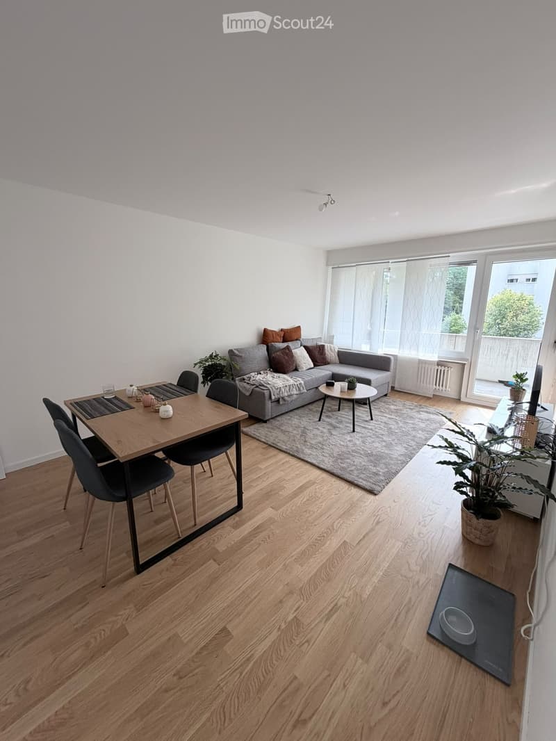 Modern living room with grey sectional sofa, wooden dining table, chairs, coffee table, and plants.