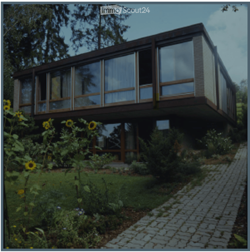 Modern two-story house with large windows, a balcony, and a well-maintained garden with sunflowers and shrubs.