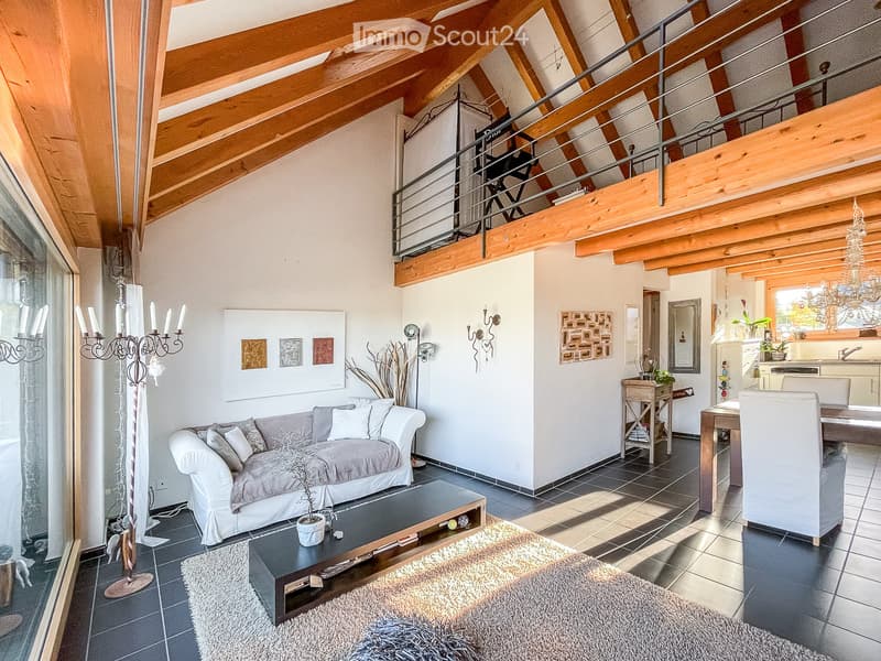 Spacious living room with exposed wooden beams, a grey sofa, coffee table, dining area, and modern decor including a chandelier and artwork.
