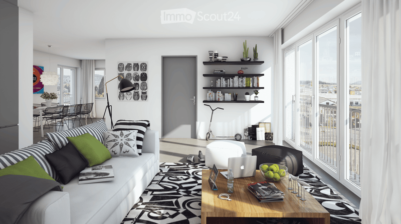 Modern living room with large windows offering a city view, white sofa with colorful pillows, wooden coffee table, laptop, ottoman, and bookshelf with decorative items.