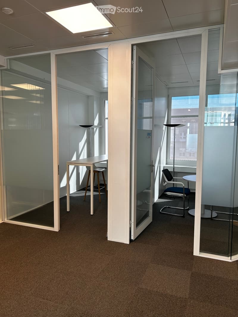 Modern office space with glass partitions, a small table with a chair, a stool, and a floor lamp in the corner.