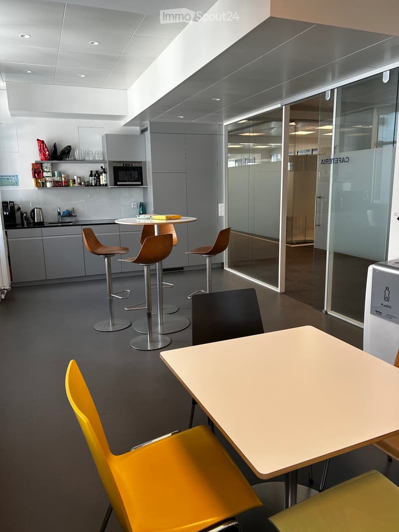 Modern break room with grey cabinets, a microwave, sink, and various seating options including stools and chairs around tables.