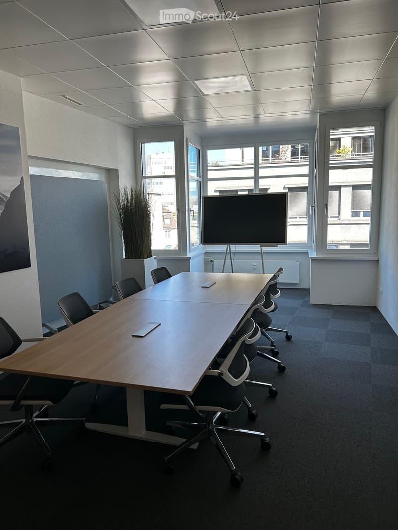 Modern conference room with a long wooden table, several chairs, a large screen, and large windows with a city view.