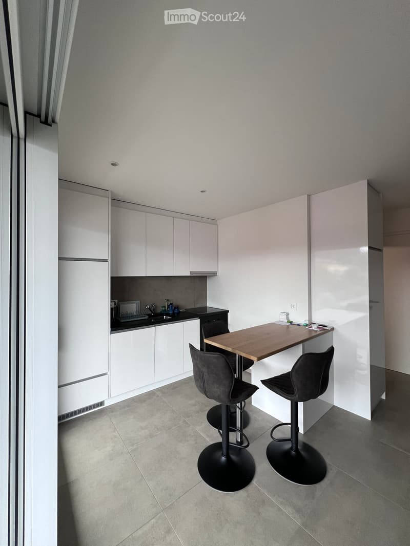 Modern kitchen with white cabinets, a wooden countertop, and two black stools.