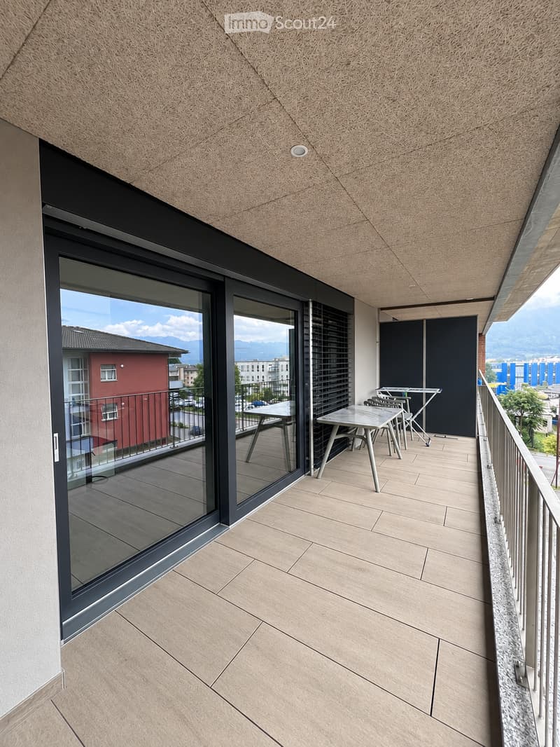Modern balcony with light-colored tiled flooring, large glass sliding doors, and a small seating area with a table and chairs.