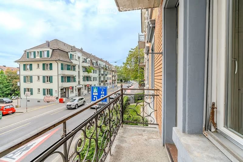 Balcony overlooking a street with multi-story buildings, cars, and a parking sign visible.