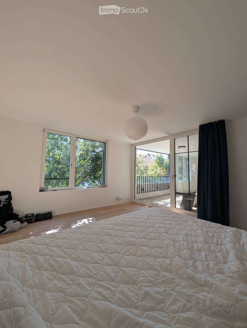 Bright bedroom with large windows, a neatly made bed, and a pendant light fixture.