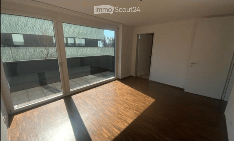 Empty room with wooden flooring, large sliding glass doors leading to a balcony, and white walls.