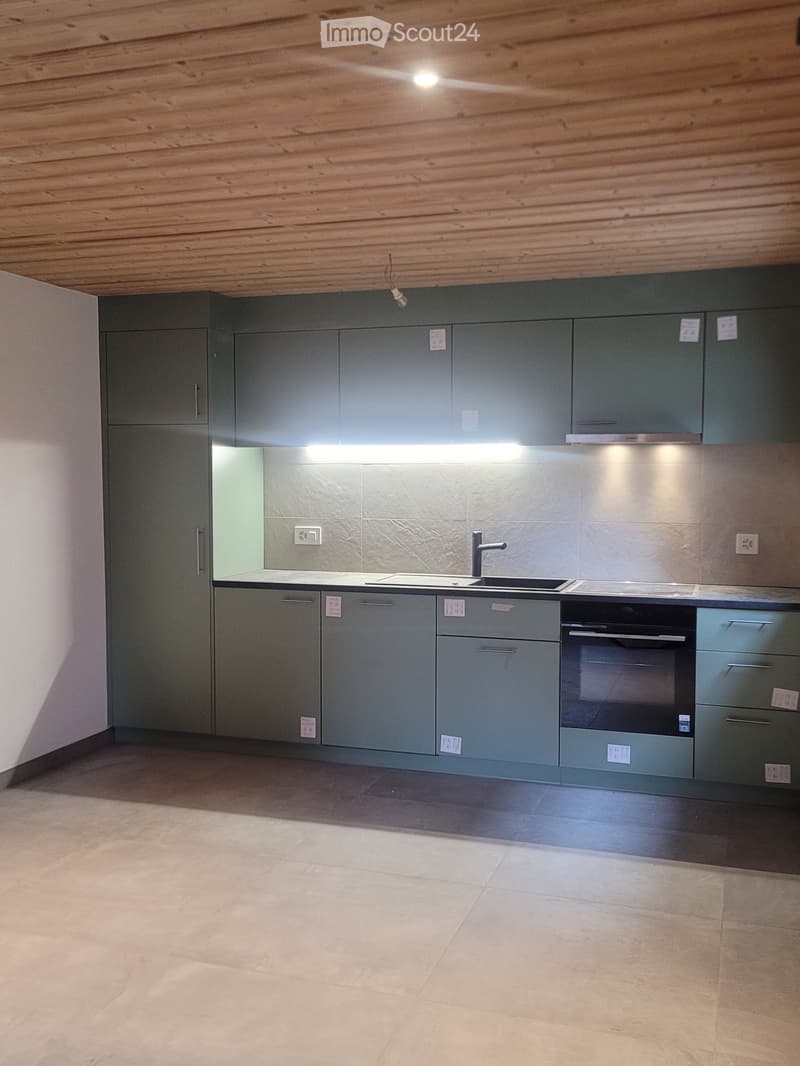Modern kitchen with grey cabinets, a sink, a faucet, and an oven. The space features a wooden ceiling and tiled flooring.