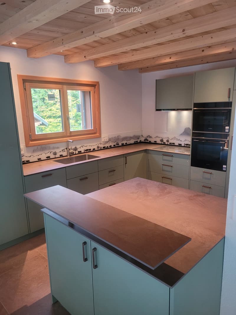Modern kitchen with light grey cabinets, a central island with a copper countertop, and a sink with a faucet. The backsplash features a mountain and cow design.