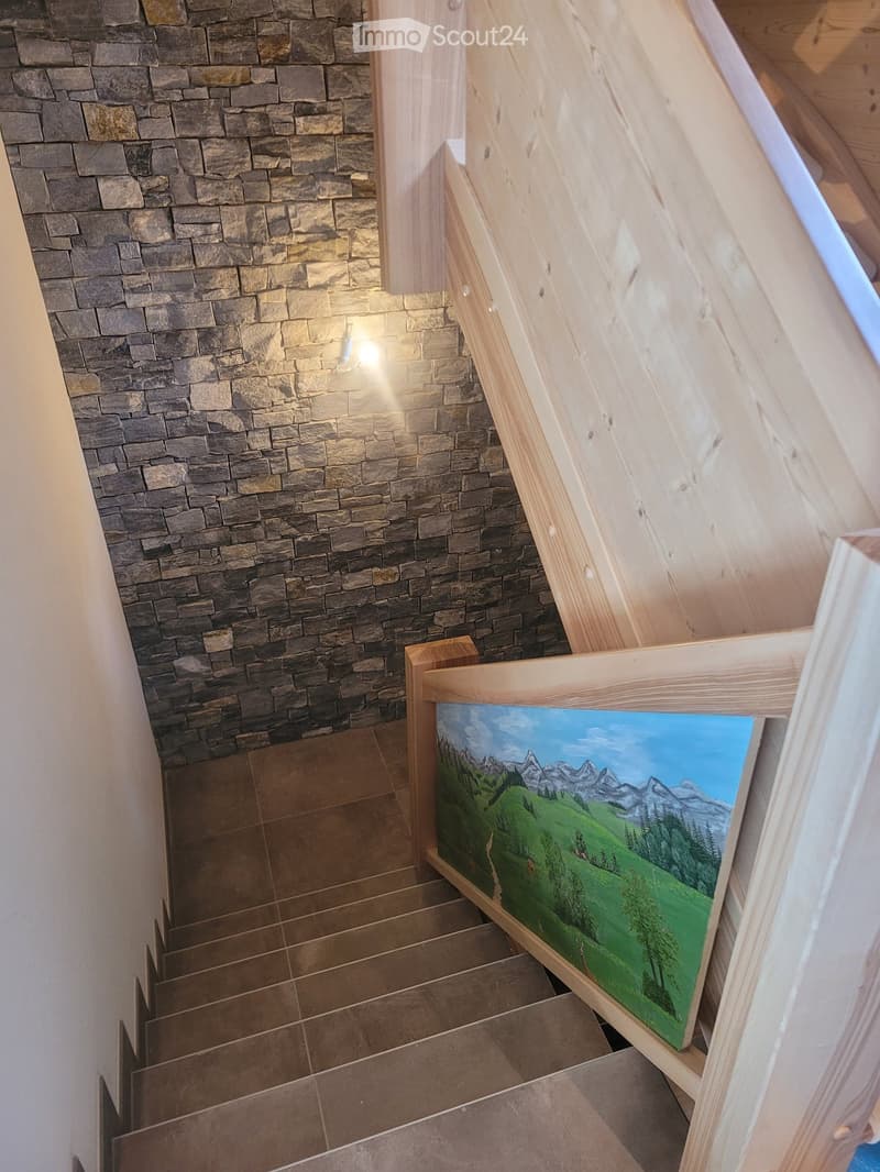 Staircase with wooden handrails and stone walls, featuring a painted mural of a mountain landscape on the landing.