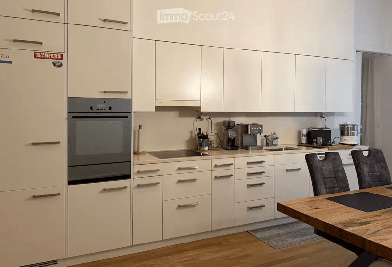 Modern kitchen with white cabinets, stainless steel appliances, and a wooden dining table with chairs.