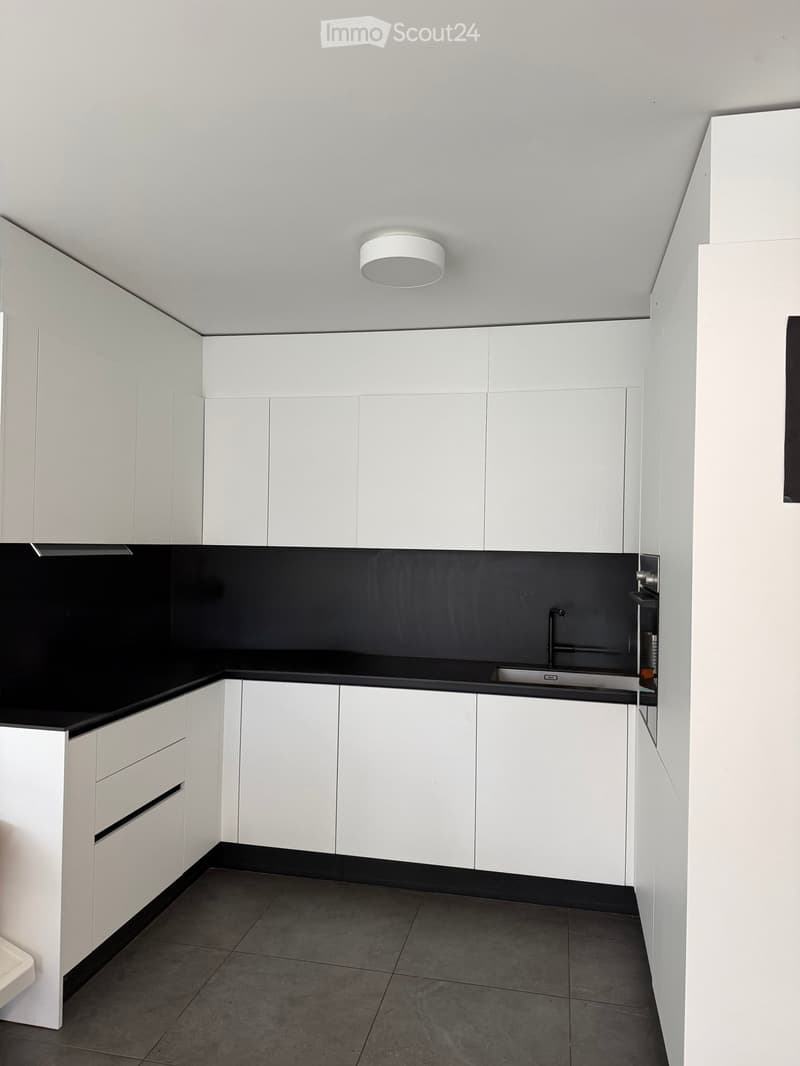 Modern kitchen with white cabinets, black countertops, and a stainless steel sink.