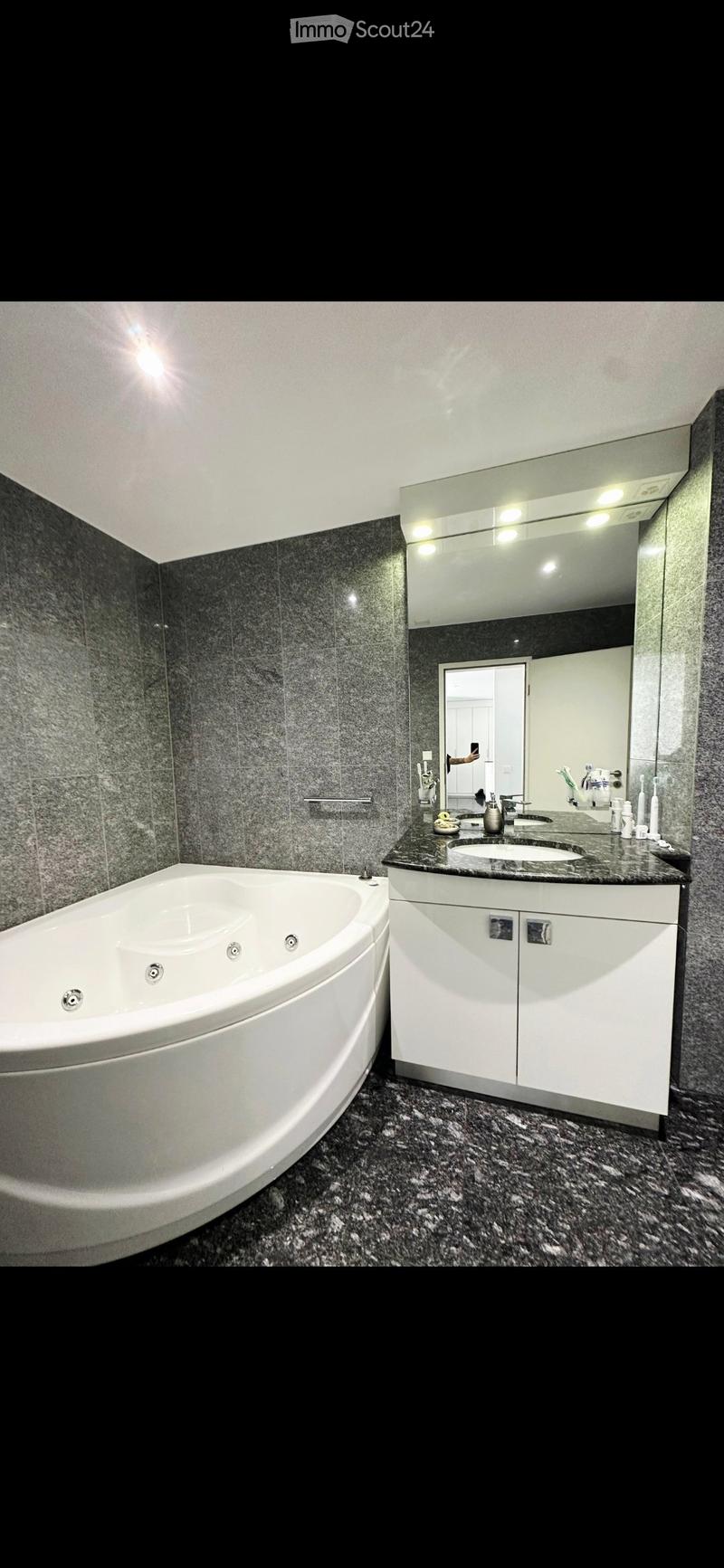 Modern bathroom with a large bathtub, double sink vanity, mirrored cabinet, and granite countertops.
