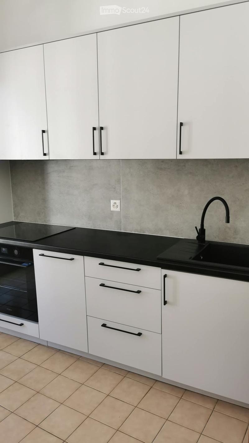 Modern kitchen with white cabinets, black countertop, built-in oven, and sink with a modern faucet.