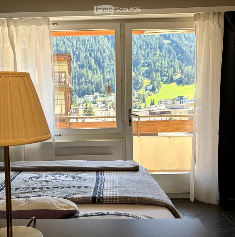 Cozy bedroom with a double bed, patterned bedding, a table lamp, and large windows offering a scenic mountain view.