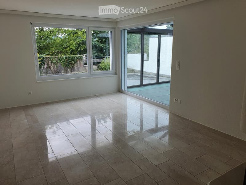 Empty room with large windows and a sliding glass door leading to a patio, featuring polished tile flooring and neutral-colored walls.