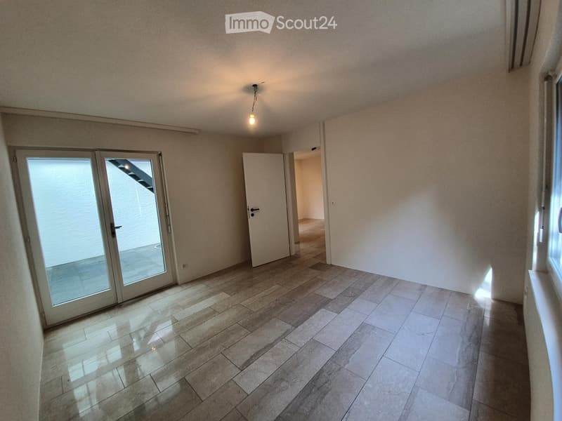 Empty room with tiled floor, white walls, and a sliding glass door leading to another space.