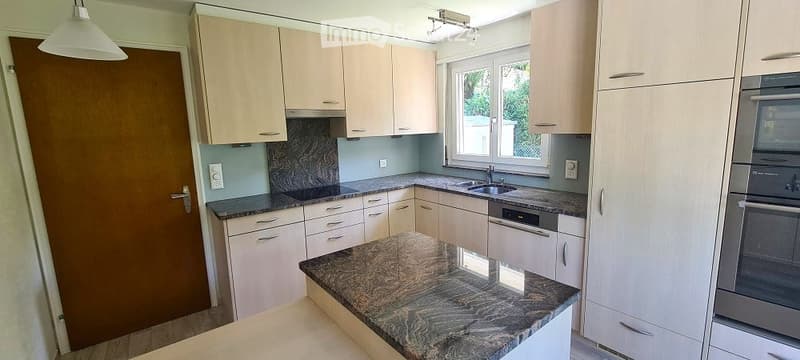 Modern kitchen with light wood cabinets, granite countertops, stainless steel appliances, and a window above the sink.