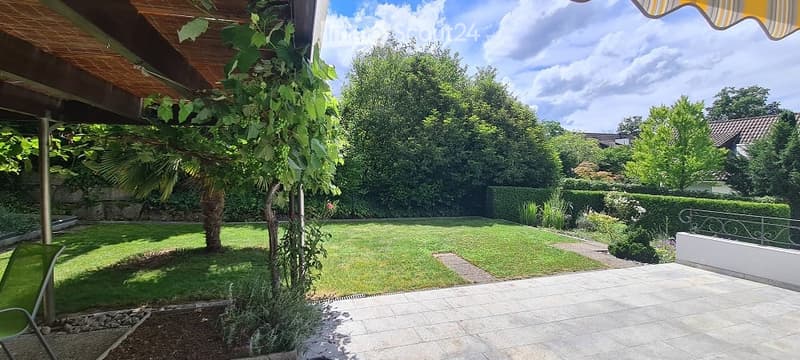 Well-maintained garden with a lawn, trees, shrubs, and a patio area with a covered seating space.