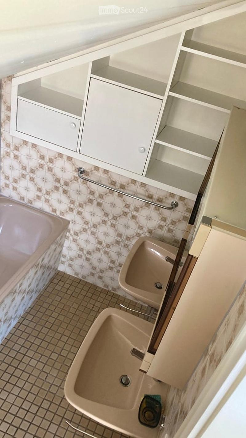 Bathroom with beige tiles, a pink bathtub, two sinks, and white cabinets with shelves.