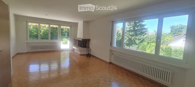 Empty room with wooden flooring, large windows, fireplace, and radiator. No furniture or equipment present.
