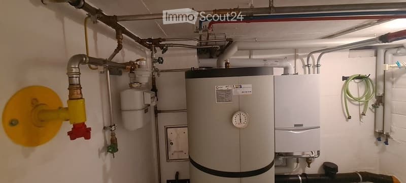 Utility room with a water heater, thermostat, and various pipes and fittings.