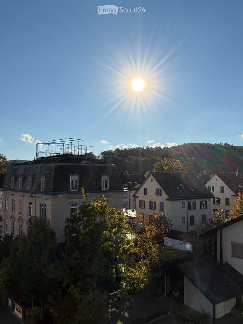 A view of a residential area with multiple buildings, trees, and a clear blue sky with the sun shining brightly.