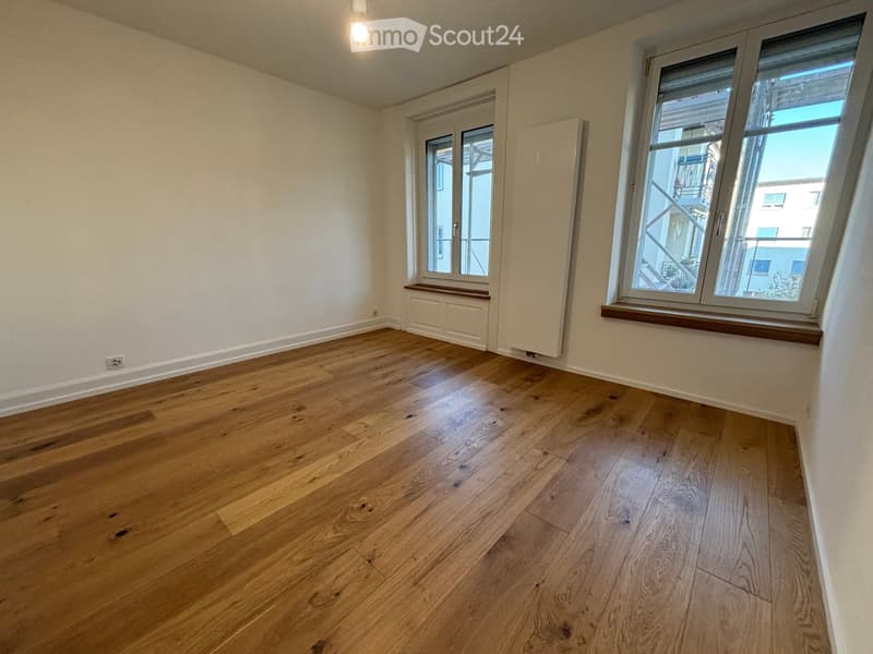 Empty room with wooden flooring, white walls, and large windows with wooden sills. No furniture or equipment present.