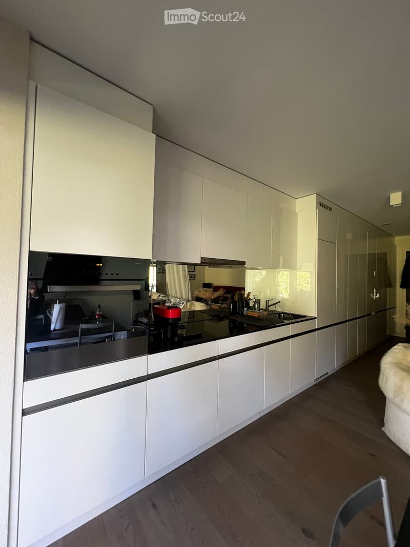 Modern kitchen with white cabinets, black countertops, and stainless steel appliances. Features a sink, faucet, oven, and coffee maker on the counter.