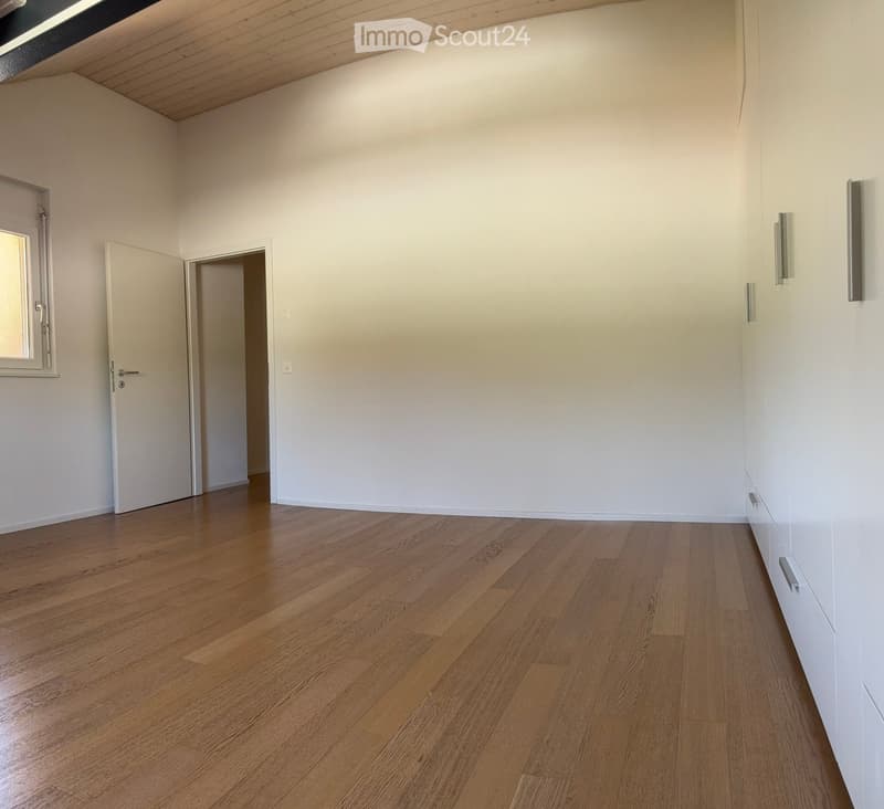 Empty room with wooden flooring, white walls, and two doors, one leading to another room and the other to a window.