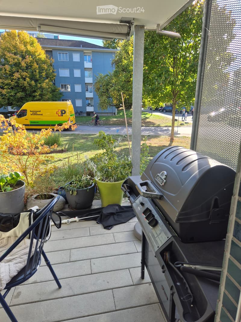 Balcony with a grill, potted plants, a folding chair, and a covered area with a retractable awning.