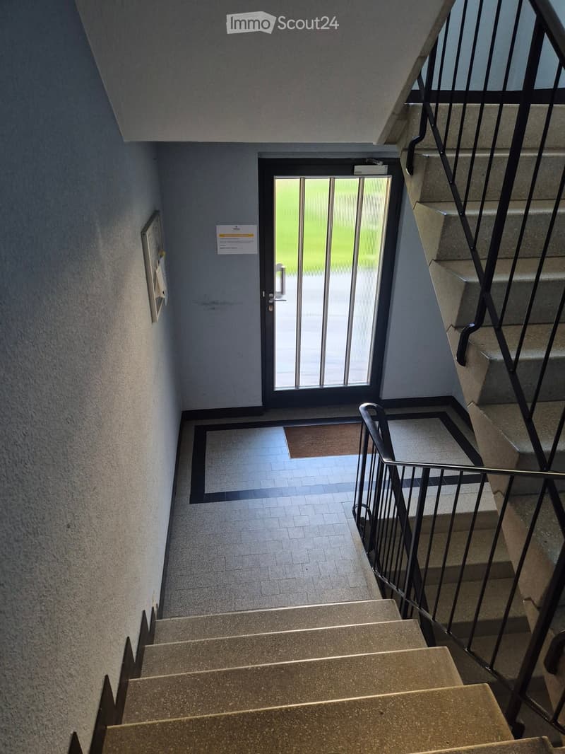 Staircase with gray steps, metal railing, and a door leading outside with a glass panel.