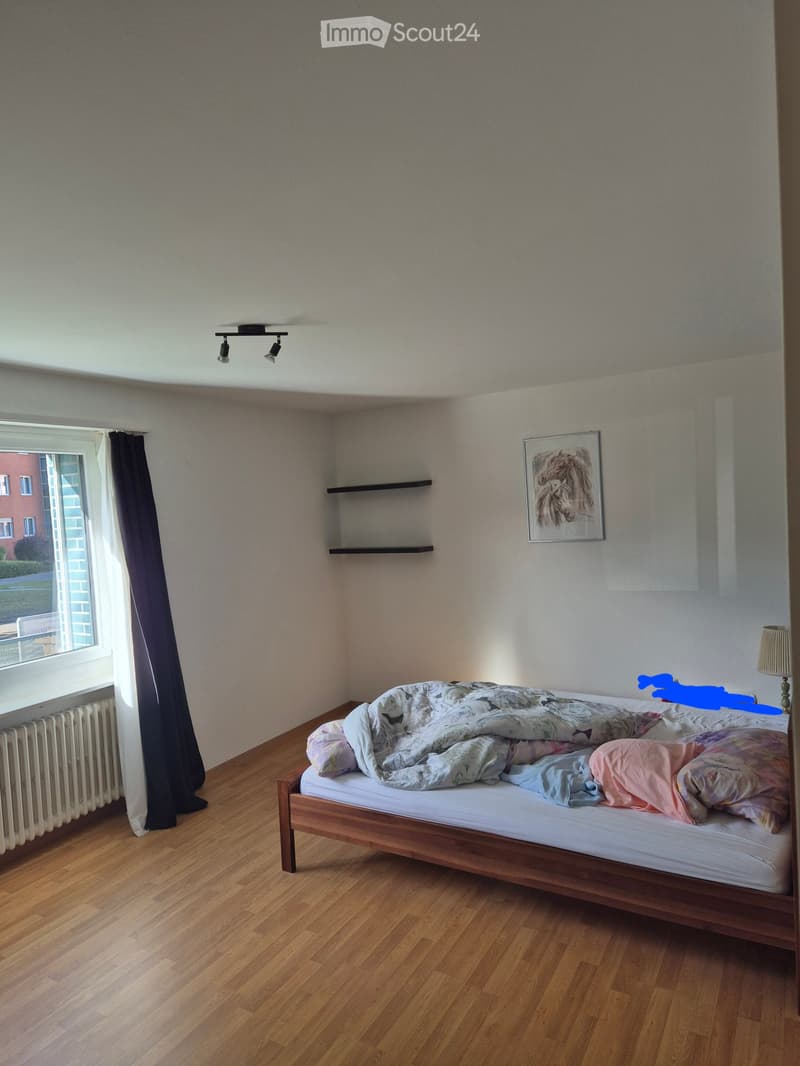 A small bedroom with wooden flooring, a single bed with blankets, a radiator, a shelf, a picture frame, and a lamp.