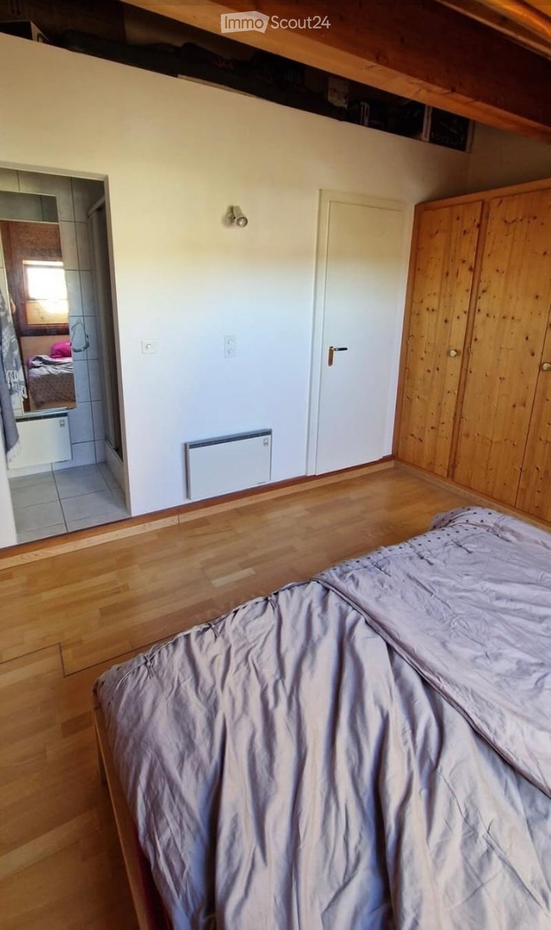 Bedroom with wooden flooring, a bed with grey bedding, a wooden wardrobe, and a visible adjacent bathroom area.