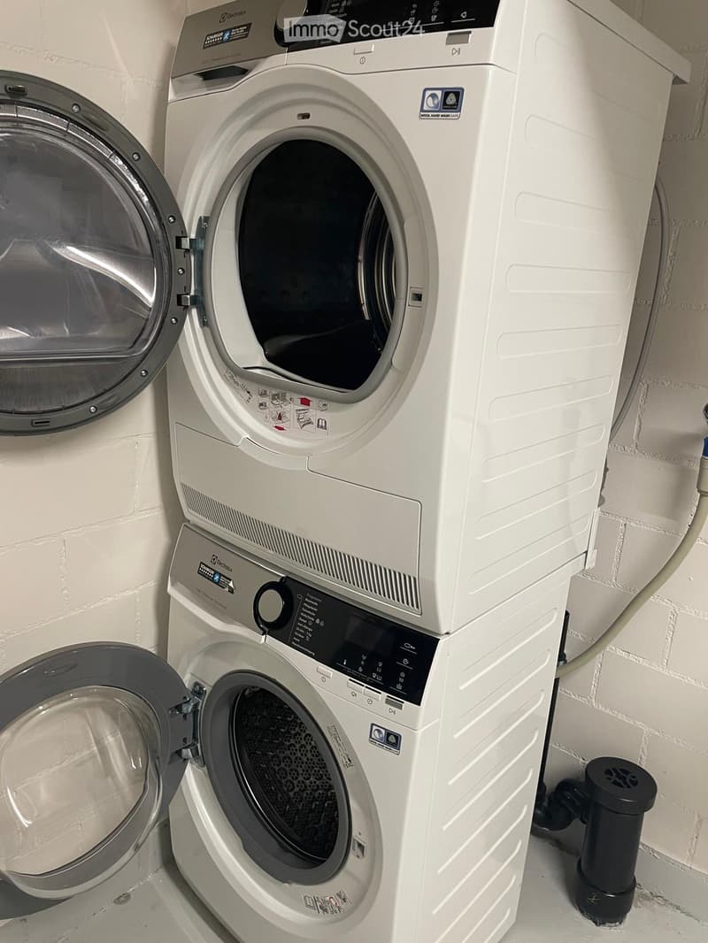 A compact bathroom with a stacked washing machine and dryer unit, both white with control panels and open doors.