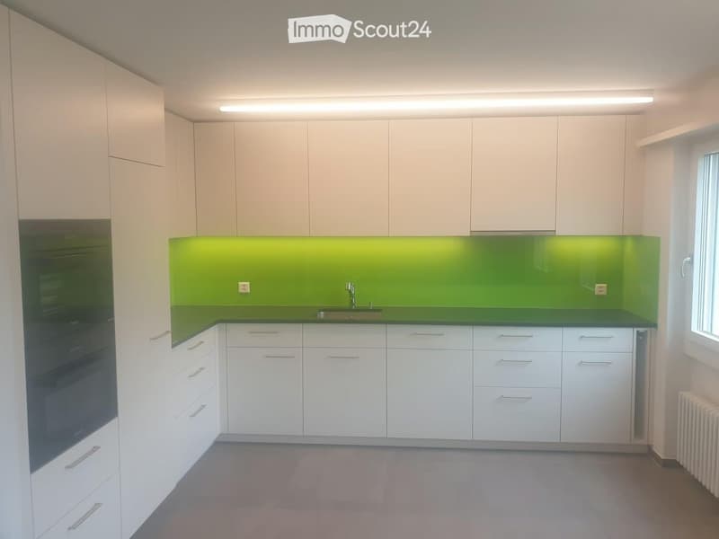 Modern kitchen with white cabinets, green backsplash, and stainless steel sink.