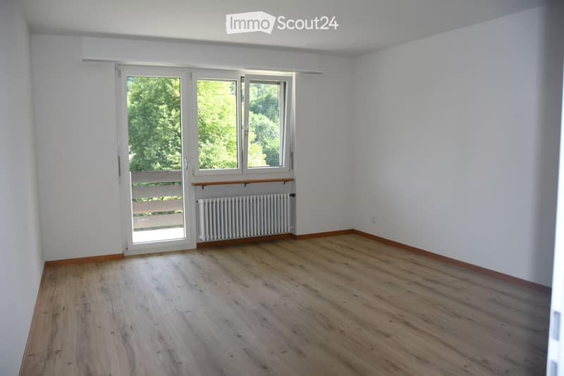Empty room with wooden flooring, white walls, large windows, and a radiator. No furniture or equipment present.