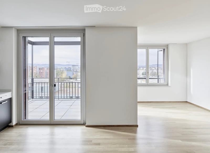 Empty room with light wooden flooring, white walls, large sliding glass doors leading to a balcony, and a window with a view of the city.
