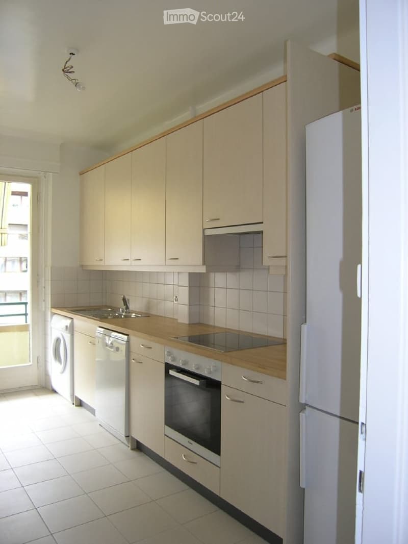 Modern kitchen with light wood cabinets, white tiles, and stainless steel appliances including a refrigerator, oven, dishwasher, and washing machine.