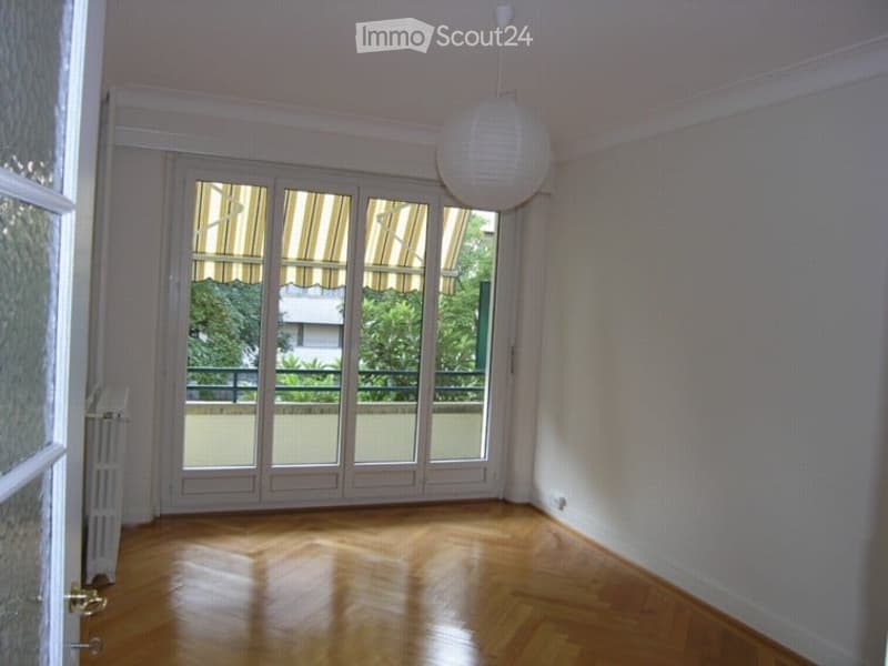 Empty room with wooden flooring, large glass doors leading to a balcony, white walls, and a hanging light fixture.