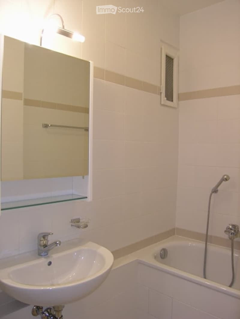 Modern bathroom with white tiles, a sink, a mirror, a bathtub, and a towel rack.