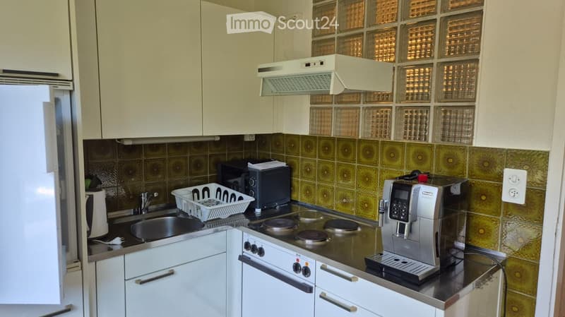 Modern kitchen with white cabinets, stainless steel appliances, and a black countertop. Features include a refrigerator, oven, coffee maker, microwave, sink, and dish rack.