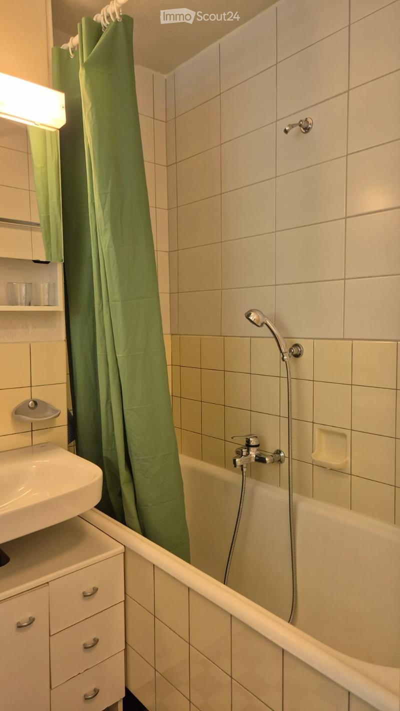 Bathroom with a bathtub, shower curtain, sink, and cabinet. The walls are tiled, and there is a mirror above the sink.