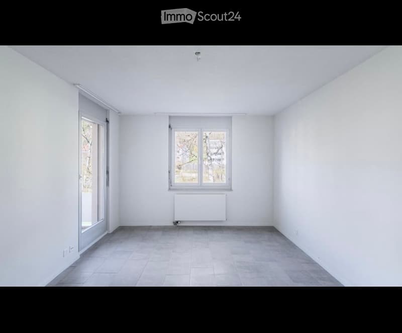 Empty room with white walls, tiled floor, and two windows, one with a radiator below it.