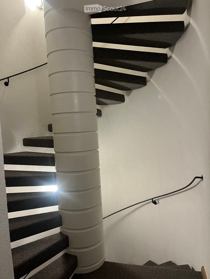 Modern staircase with black steps and a central cylindrical light fixture, white walls, and a sleek design.