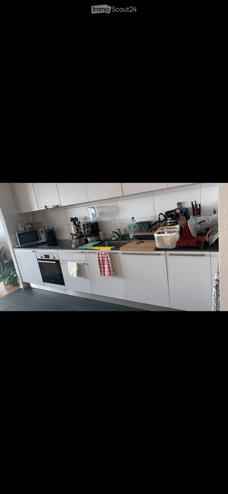 Modern kitchen with white cabinets, stainless steel appliances, and a black countertop. Visible items include an oven, microwave, sink, and various kitchen tools.