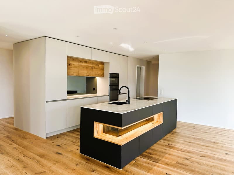 Modern kitchen with white and black cabinets, a central island with a marble countertop, a sink, and an oven. Wooden flooring and recessed lighting.