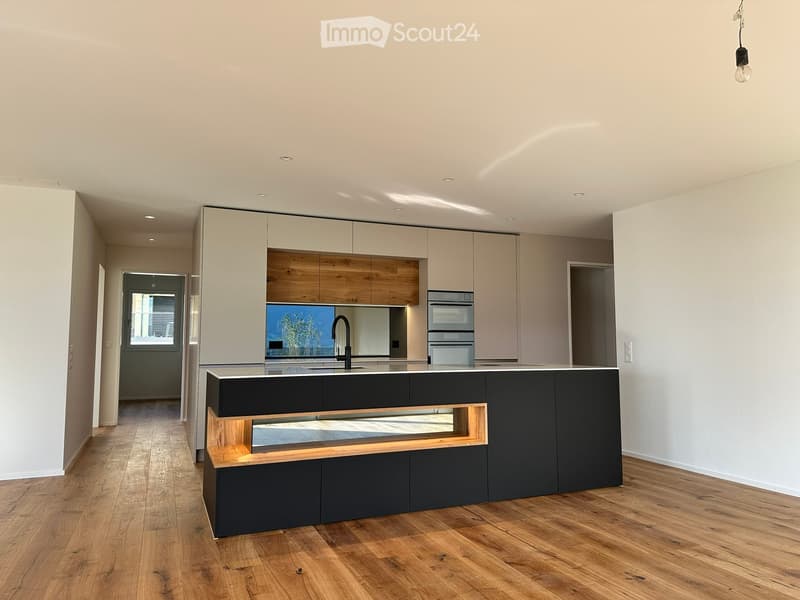 Modern kitchen with light-colored cabinets, dark lower cabinets, a central island, and a sleek sink with a modern faucet. The space features wooden flooring and recessed lighting.